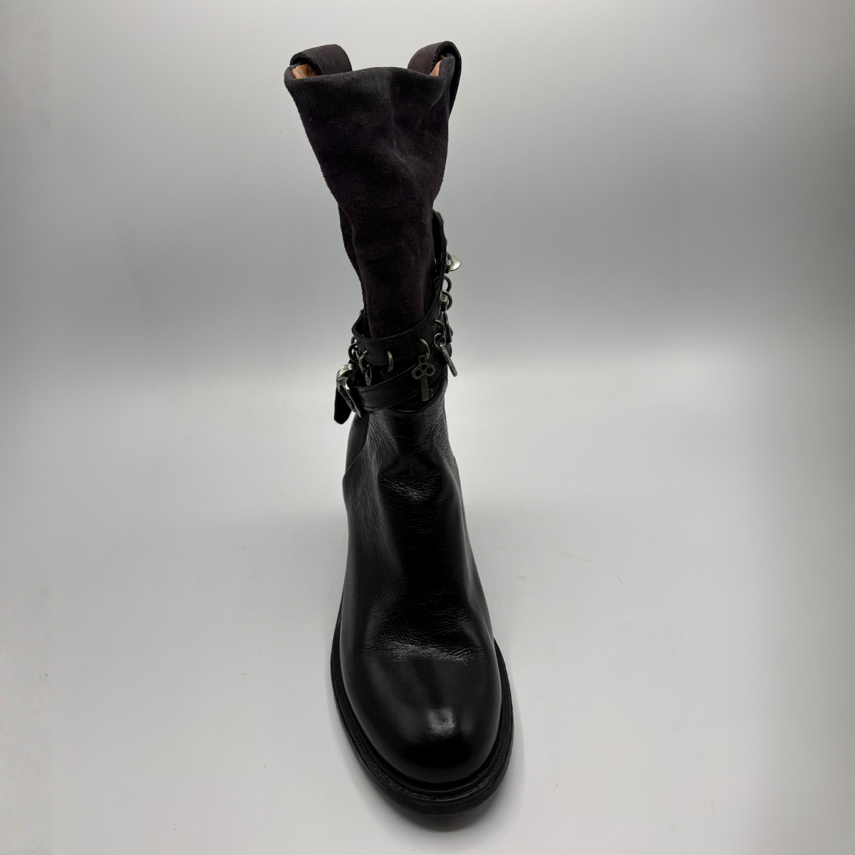 Front view of a black tall boot with a metal embellishments and a rubber outsole