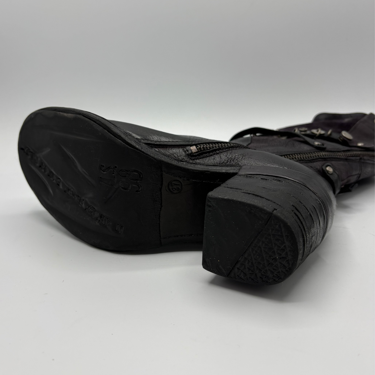 Bottom view of a black tall boot with a metal embellishments and a rubber outsole