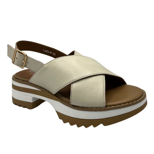 Angled view of cream leather sandals with a cross strap design, chunky sole and adjustable sling back strap.