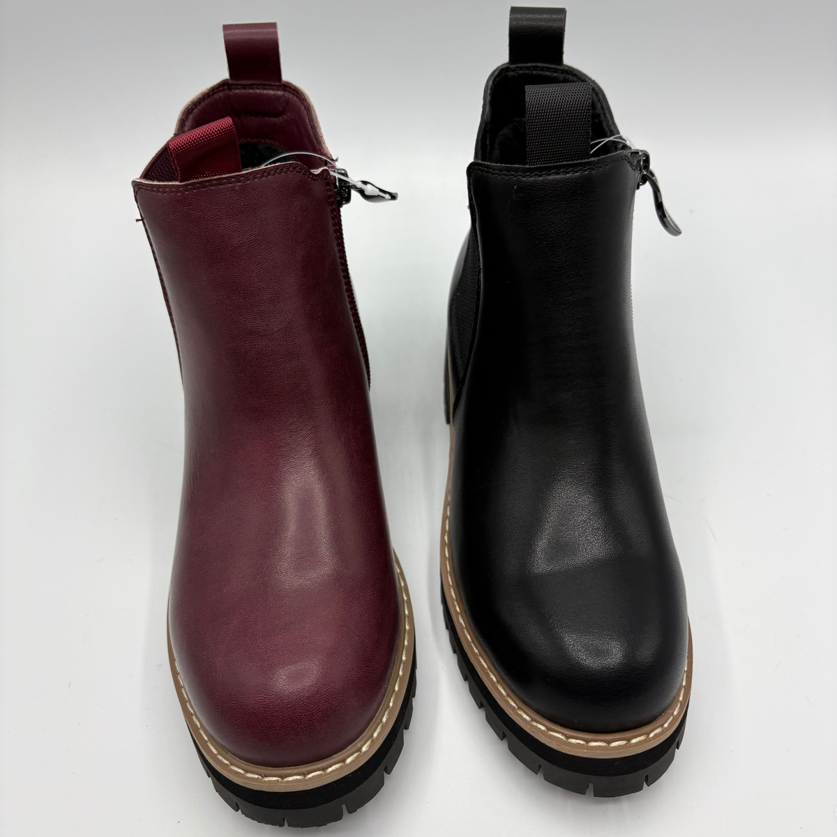 Top view of a pair of chelsea boots both with a side zipper closure. One is black and the other is plum
