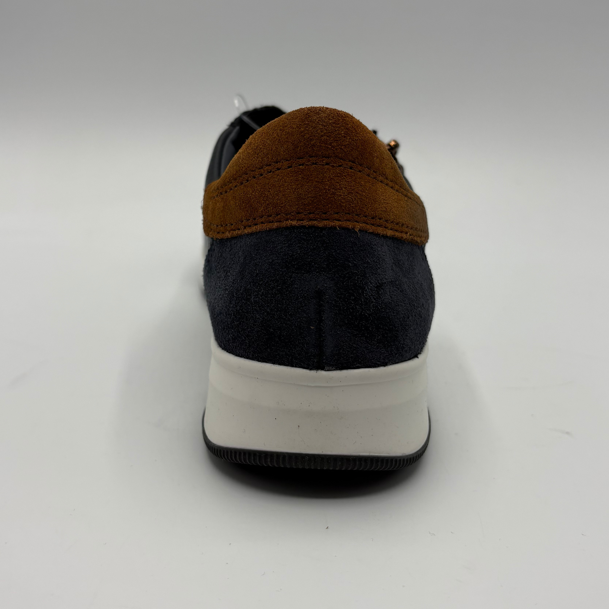 A single low-top sneaker shown from the back, featuring a dark navy blue suede upper, a contrasting brown suede heel tab, and a thick white midsole.