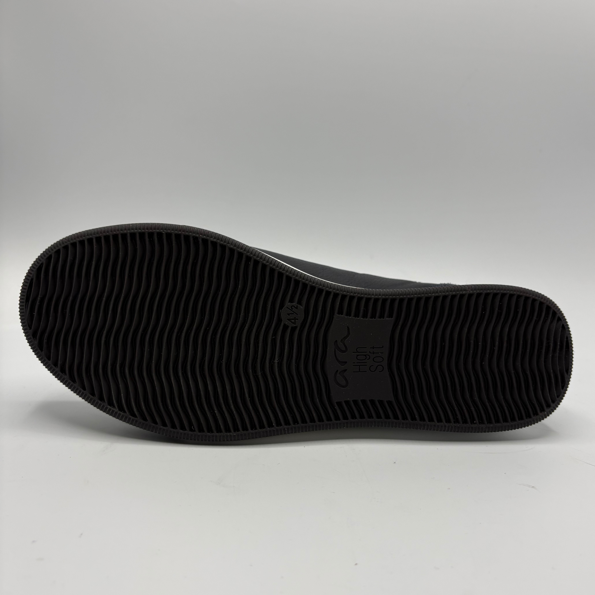 The black textured rubber outsole of a shoe, showing the embossed logo  on a light gray studio background.
