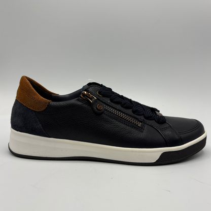 A leather low-top sneaker with a brown suede heel tab, black laces, a decorative zip detail on the side, and a thick white midsole, shown against a neutral gray background.