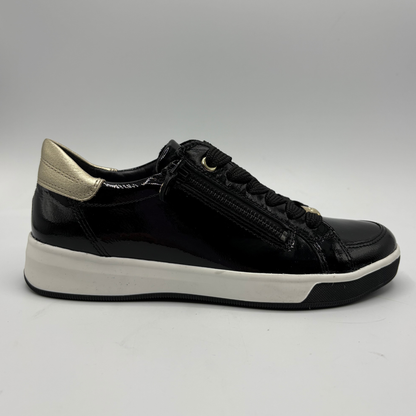 A black leather low-top sneaker with a gold metallic heel tab, black laces, a side zipper, and a thick white platform sole, shown from a side profile on a neutral gray background.