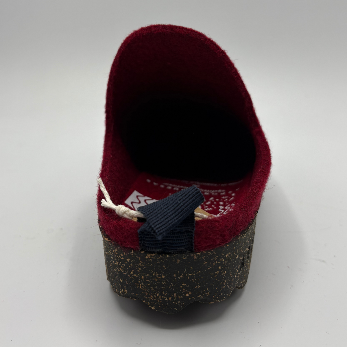 A single mule shoe shown from the back, featuring a deep burgundy felt upper, a dark navy fabric pull tab, and a textured black and brown speckled cork sole, set against a plain light gray background.
