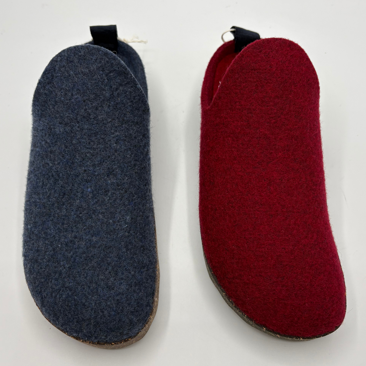 Two slip-on wool shoes side by side on a plain white background, one in dark blue-gray and one in deep red, each with a small black pull tab at the top.