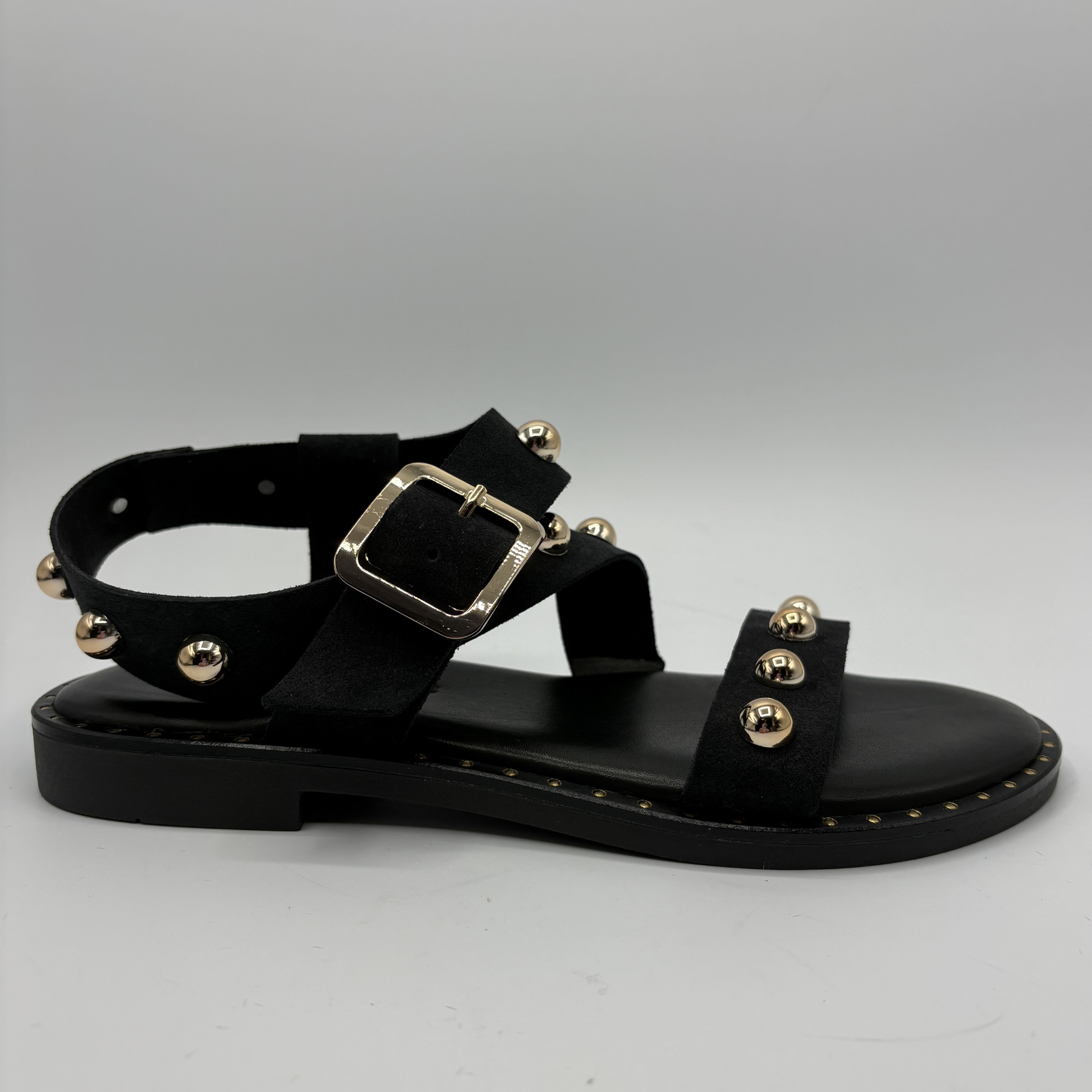 Black sandal with gold embellishments on a gray background