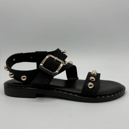 Black sandal with gold embellishments on a gray background