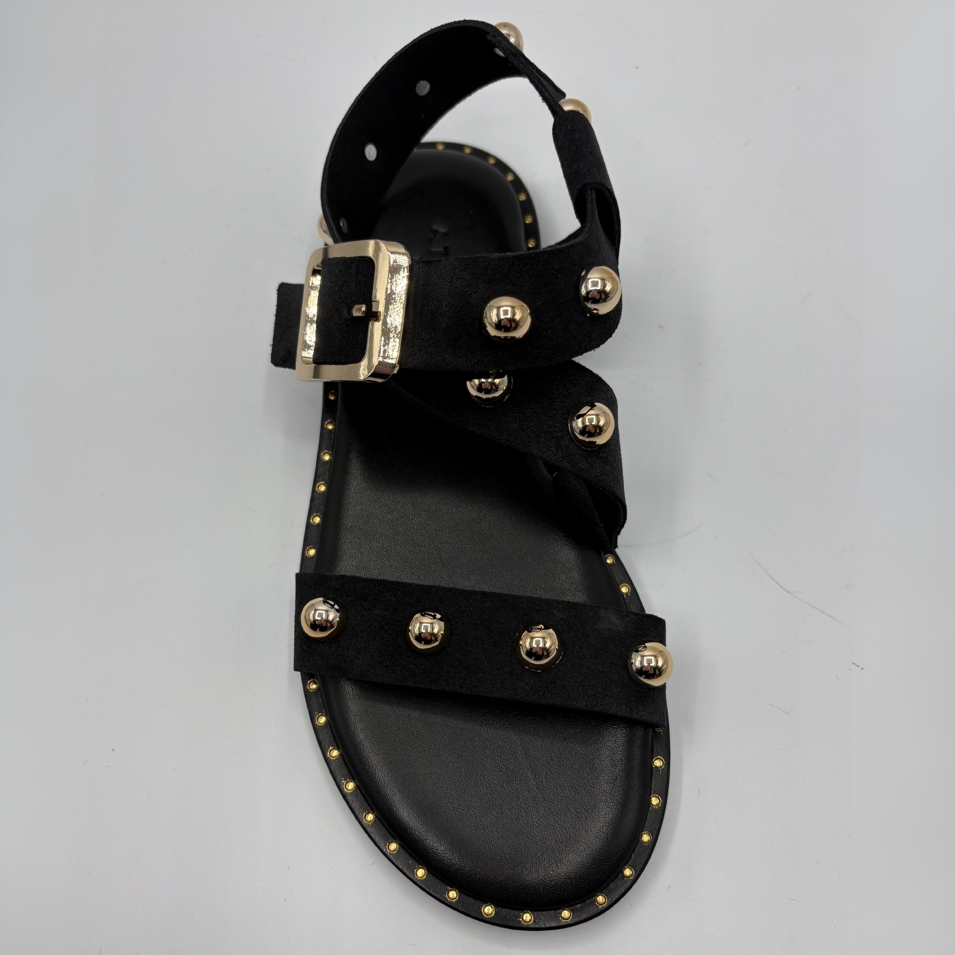 Black sandal with gold buckles and studs on a gray background