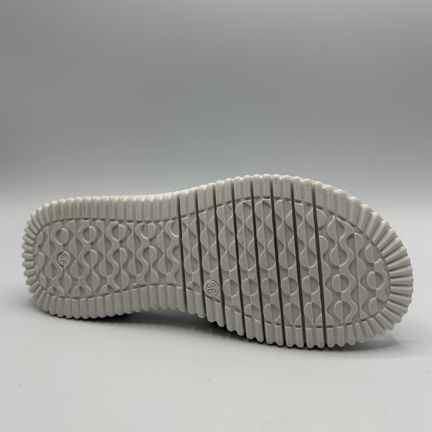 Close-up of a white sneaker sole with tread pattern on a gray background