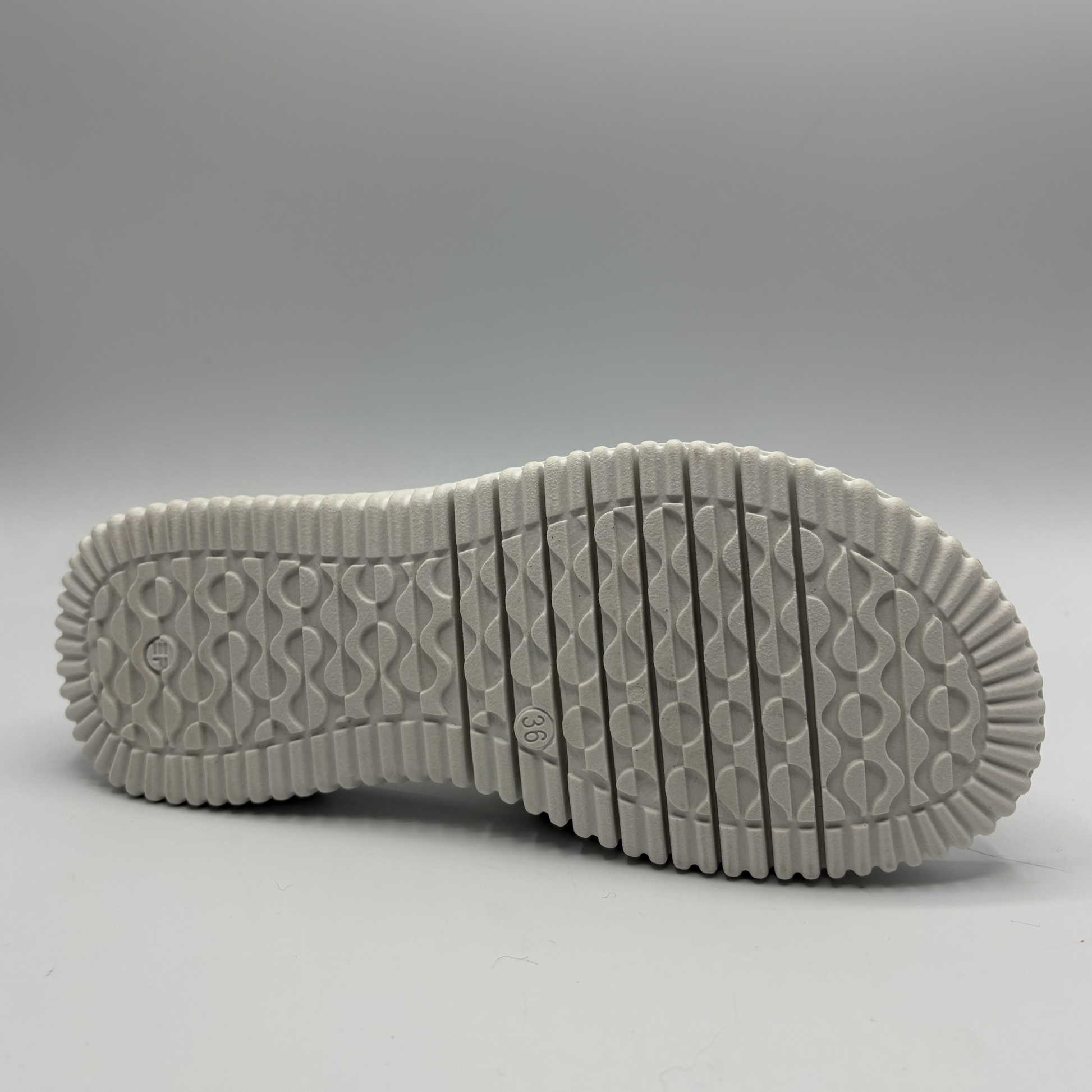 Close-up of a white sneaker sole with tread pattern on a gray background