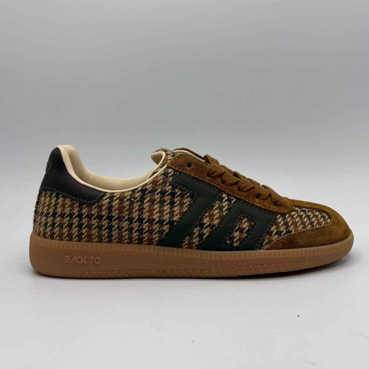 A single low-top sneaker shown in profile against a neutral gray background. The shoe features a brown and beige houndstooth pattern on the upper, dark green suede side stripes, a brown suede toe cap, and a thick brown gum sole with 'BACK 70' printed on the side.