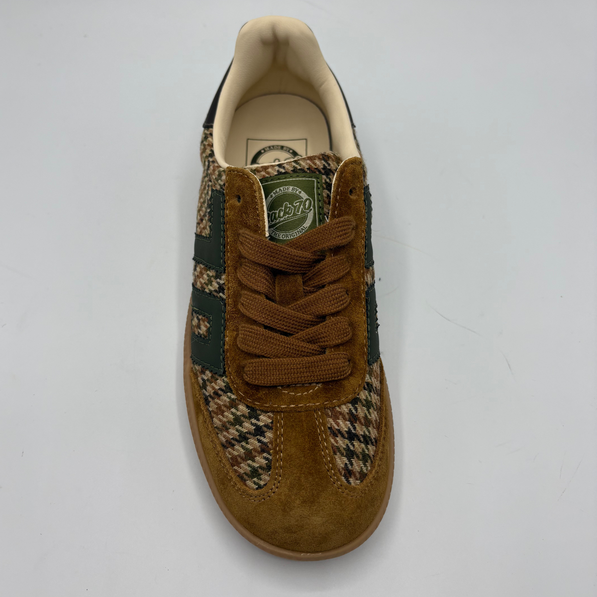 A single low-top sneaker shown from a top-down view on a light gray background. The shoe features a mix of brown suede, dark green leather panels, and a beige and black houndstooth pattern on the toe box and side stripes.