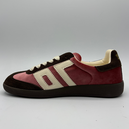 A low-top suede sneaker in pink, dark brown, and cream, shown from a side profile against a neutral gray background.
