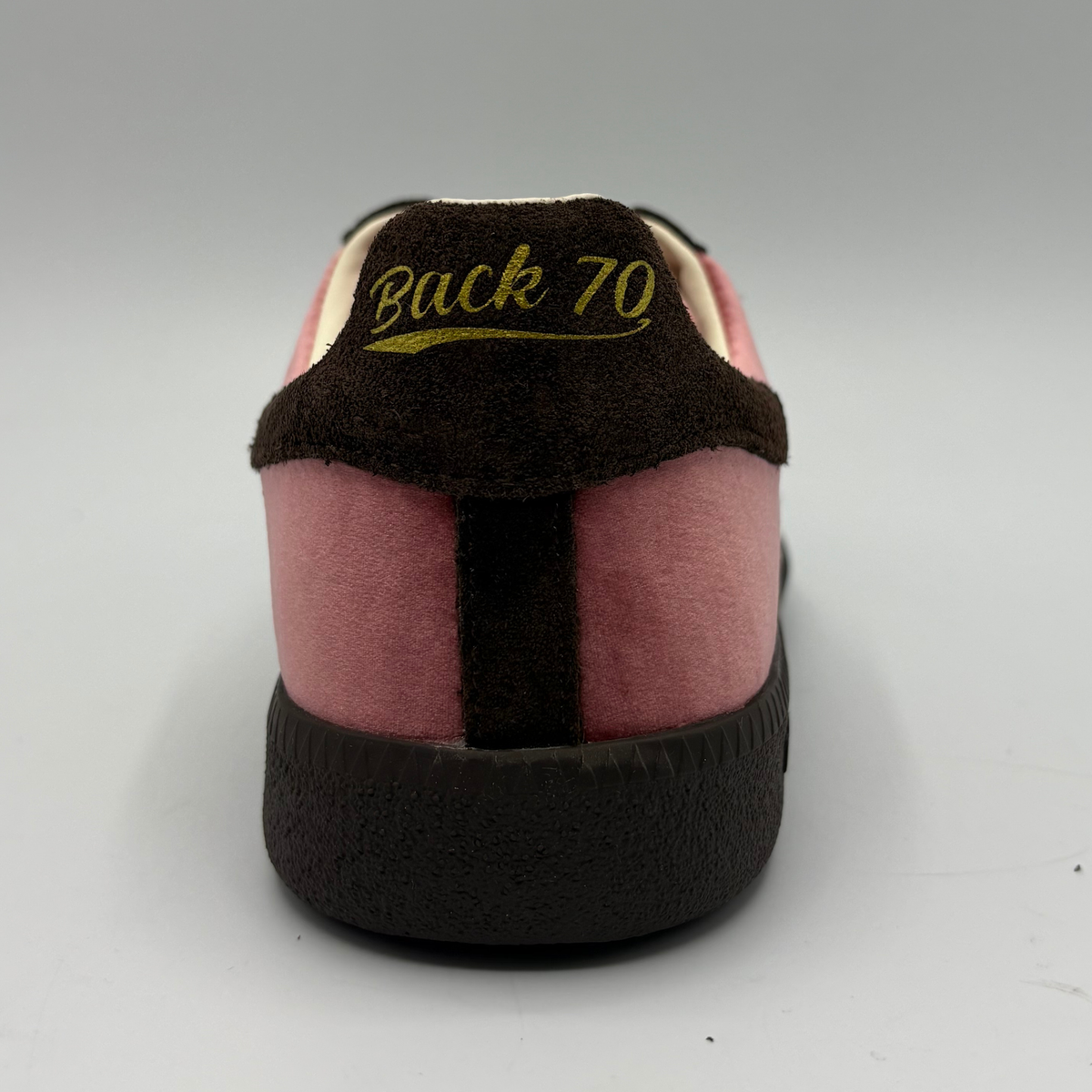 A close-up rear view of a sneaker with pink suede panels, a dark brown heel tab, and yellow text reading 'Back 70' on the heel counter.
