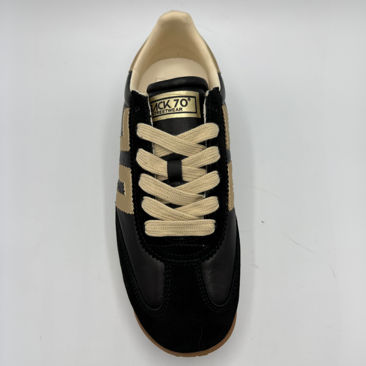 A single black and beige low-top sneaker shown from a top-down view on a light gray background. The shoe features black leather panels, beige suede overlays, beige laces, and a tan outsole.