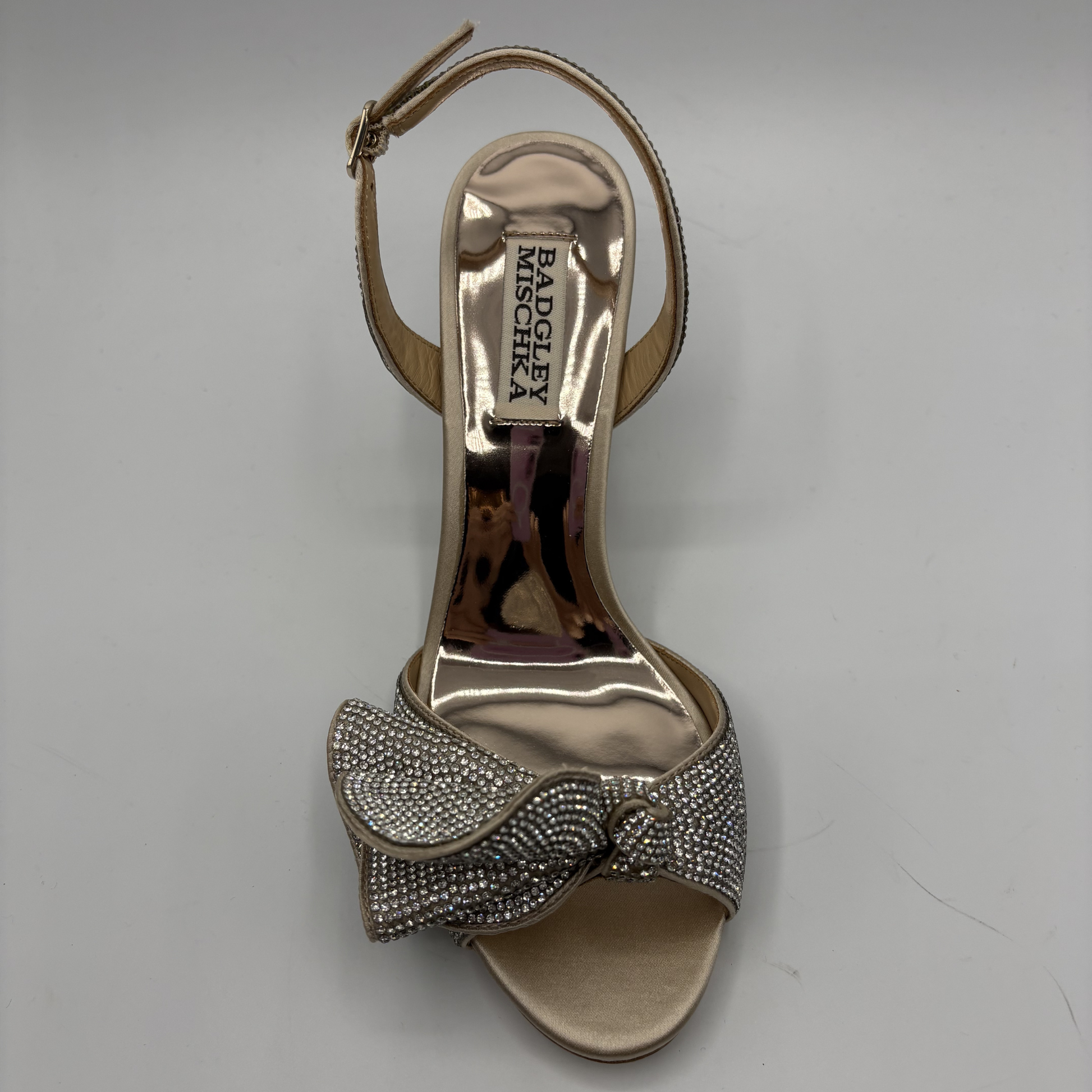 Gold high-heeled sandal with decorative bow on a gray background