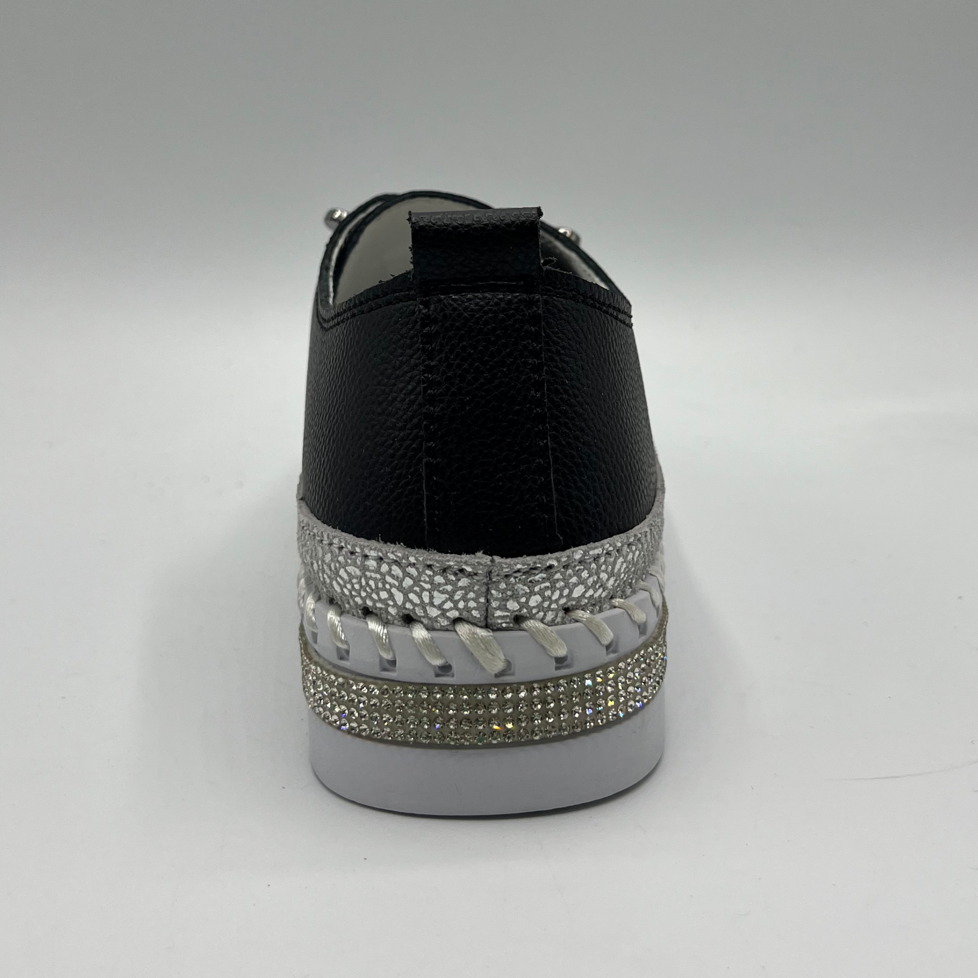 Black sneaker with silver embellishments on a gray background