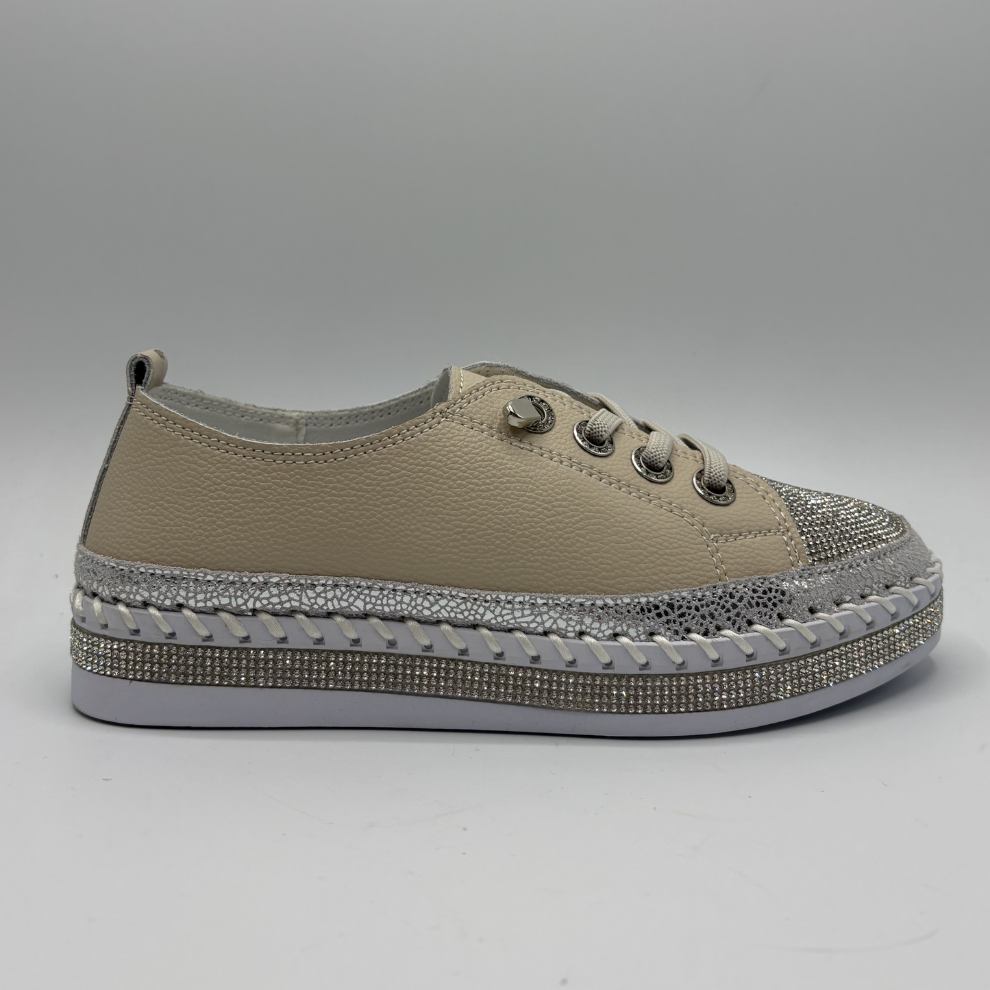 Beige sneaker with a decorative silver sole on a gray background