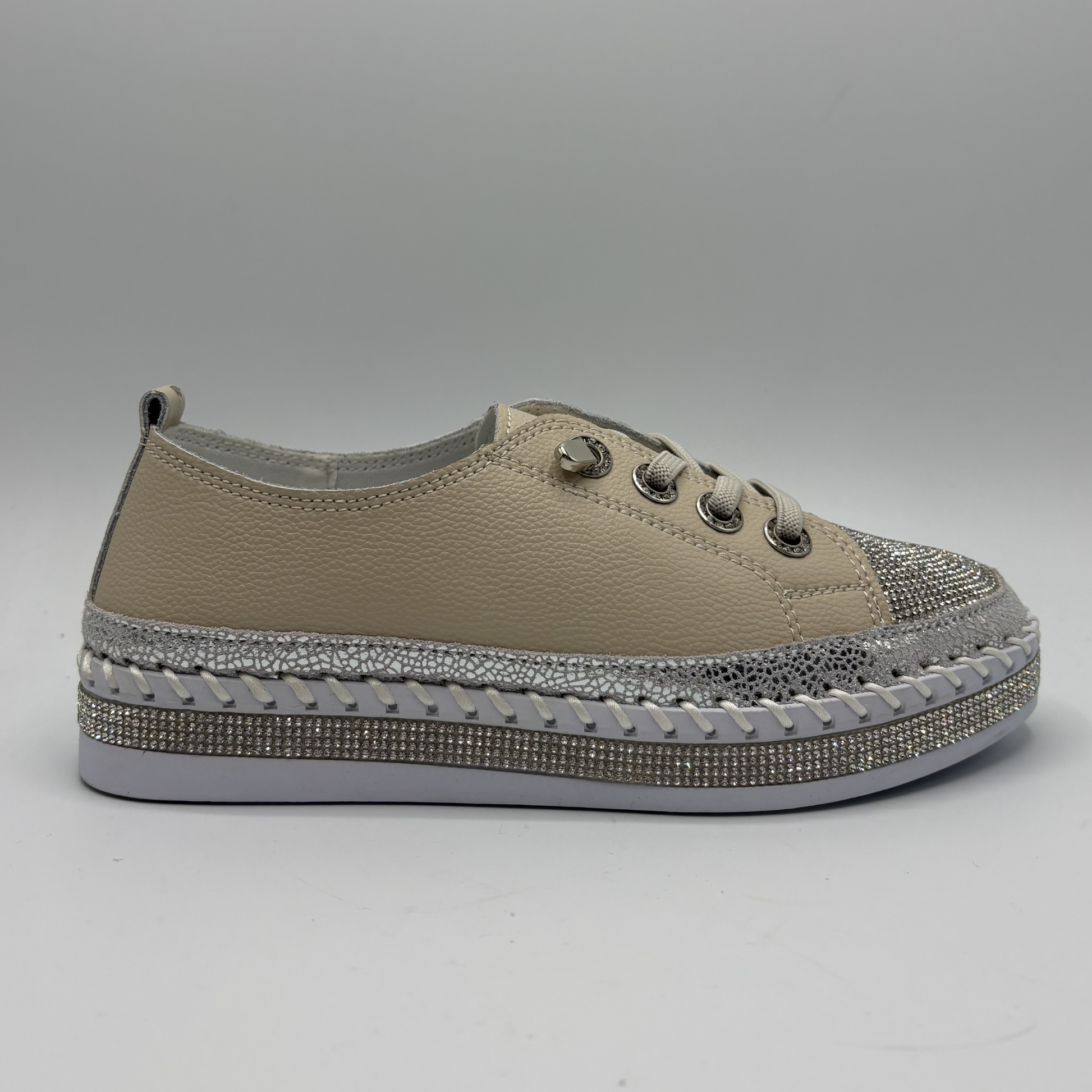 Beige sneaker with a decorative silver sole on a gray background