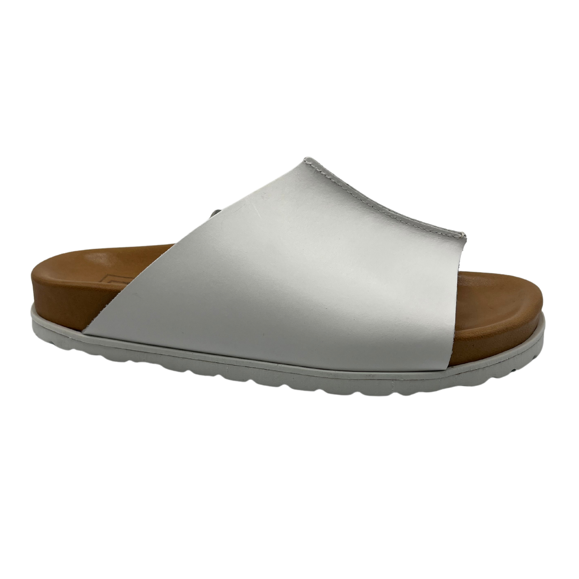 45 degree angled view of white leather slide on sandal with brown lined contoured footbed