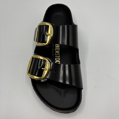 Black sandal with gold buckles on a light gray background