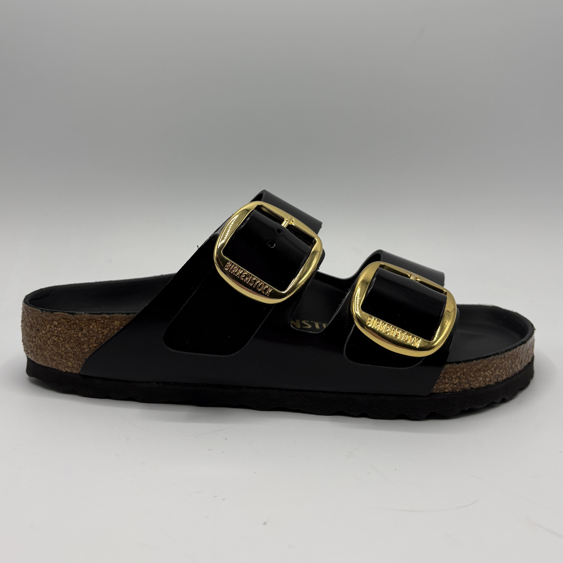 Black sandal with gold buckles on a gray background