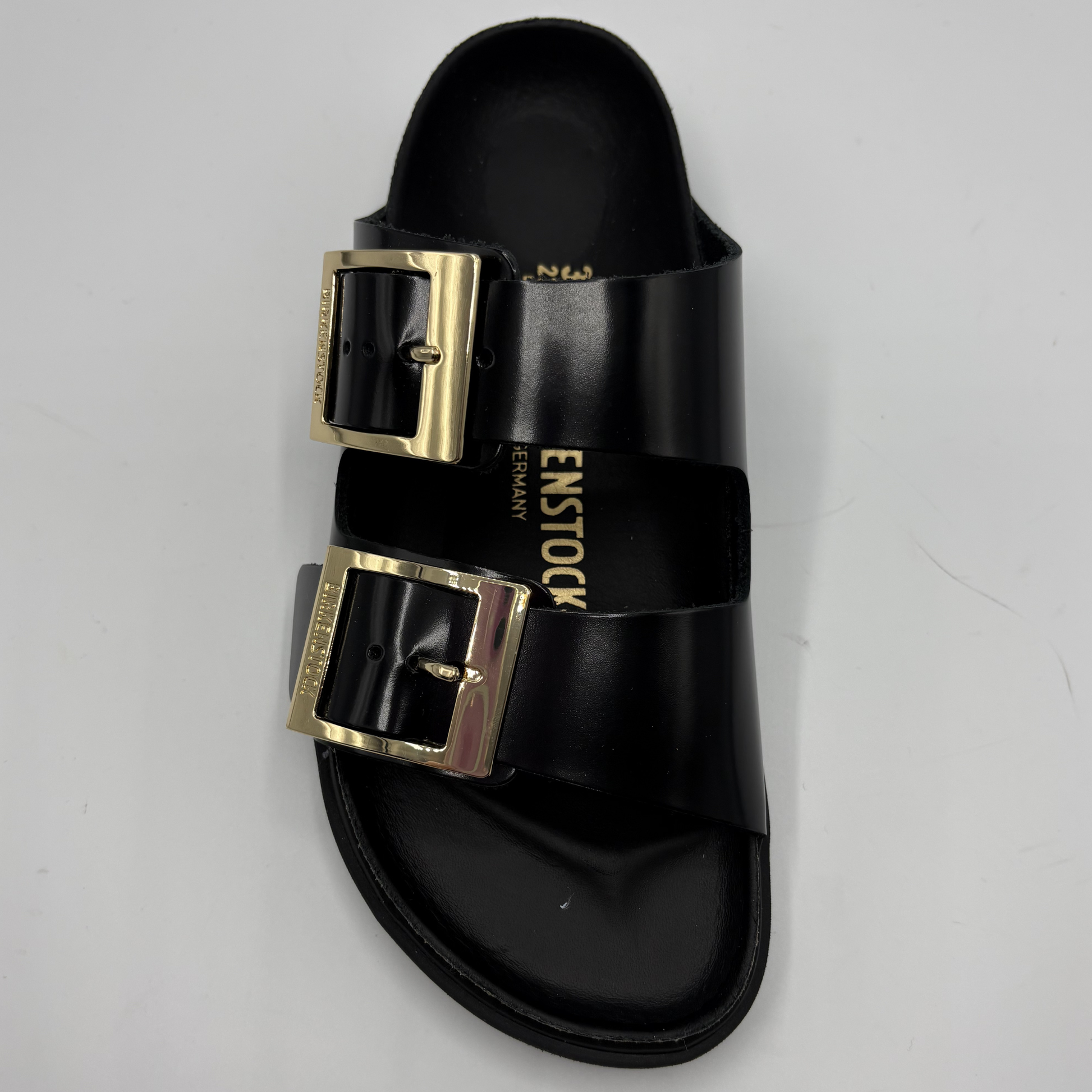 Black sandal with gold buckles on a light gray background