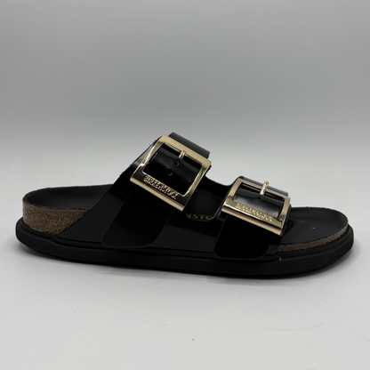 Black sandal with gold buckles on a gray background