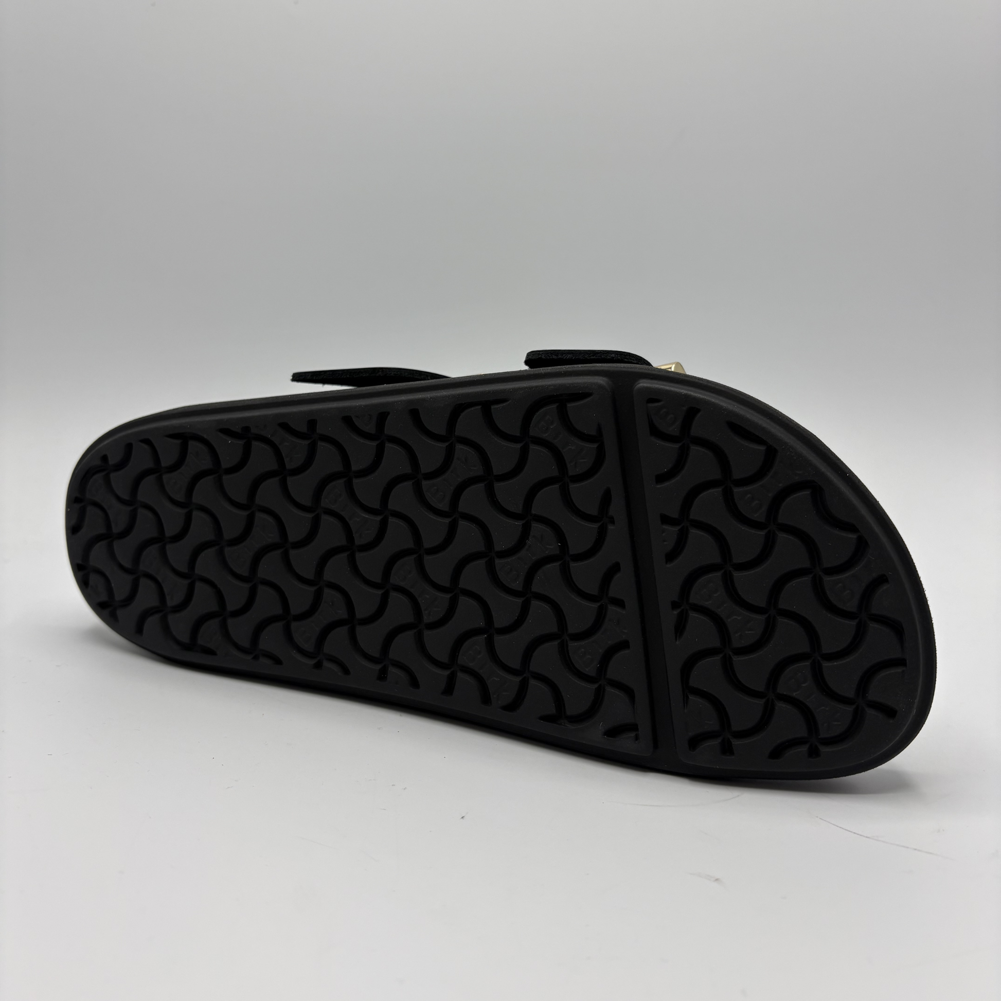 Black sandal with textured sole on a light gray background