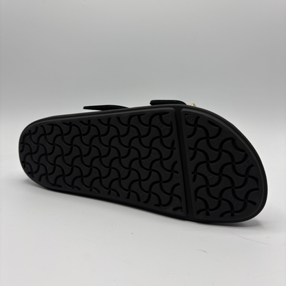 Black sandal with textured sole on a light gray background