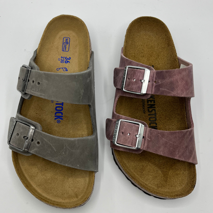 Top view of a two leather sandals side by side. Both have adjustable buckles and a contoured footbed.