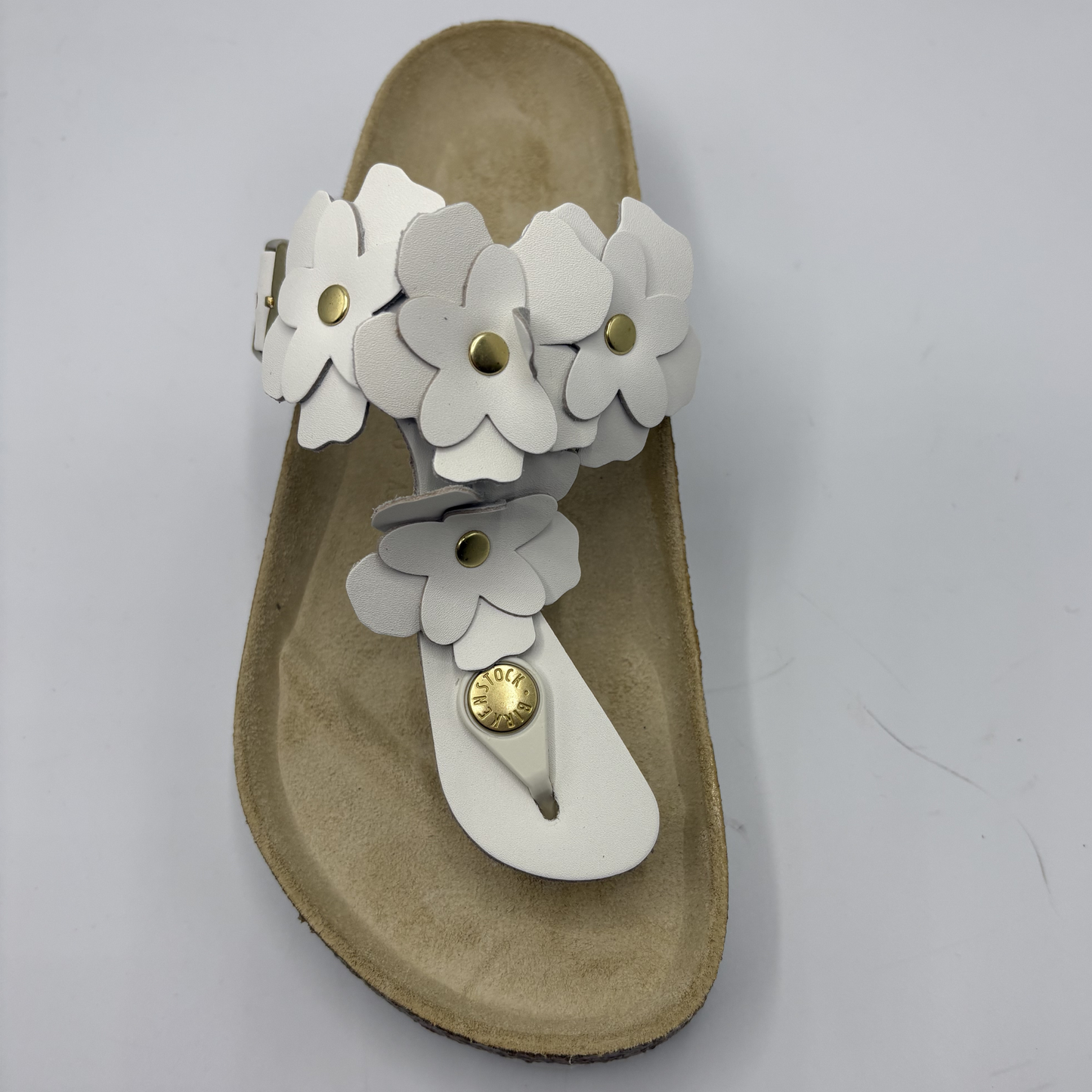 Beige sandal with white floral straps on a light gray background