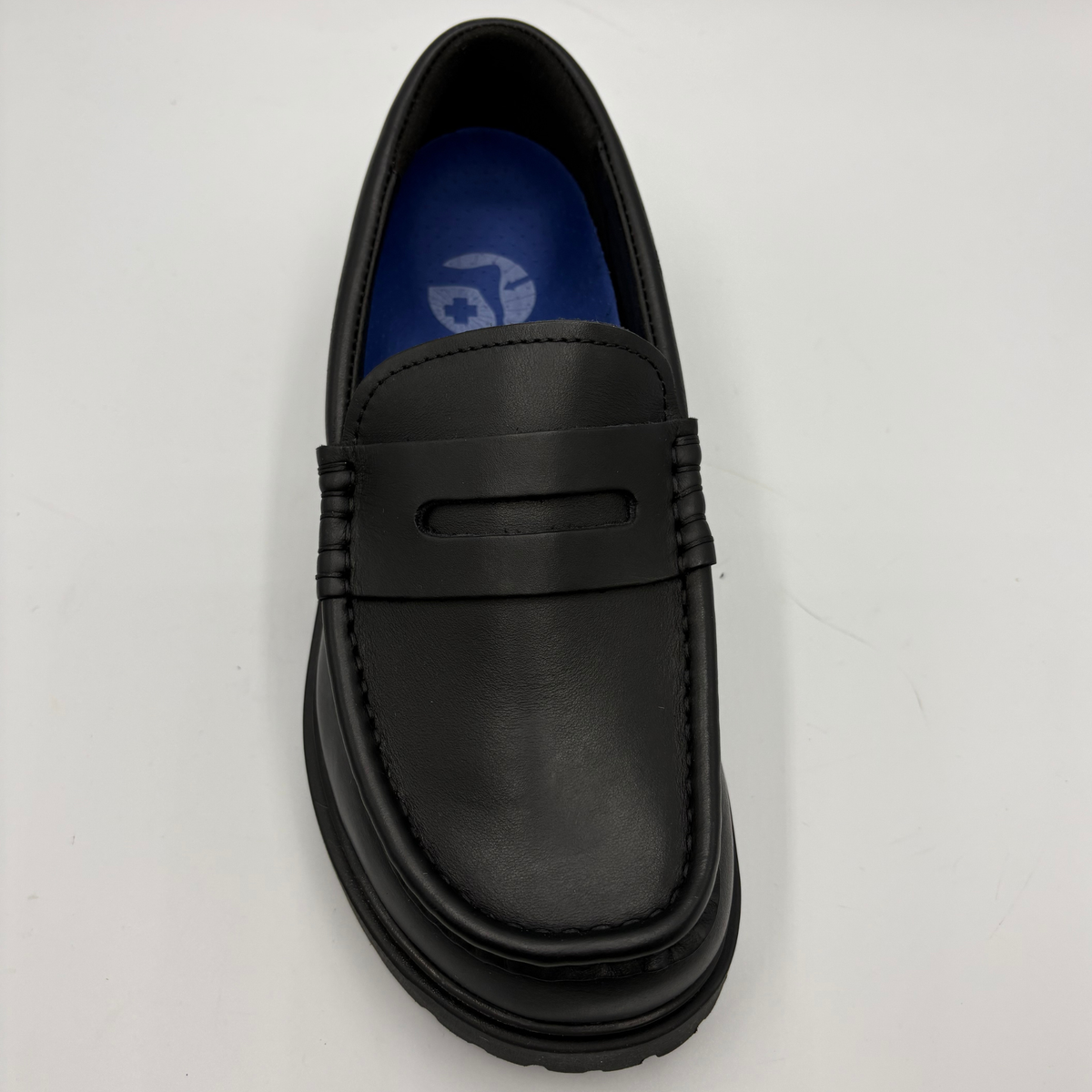 A single black leather penny loafer shoe photographed from a top-down angle on a plain white background. The shoe features a thick black sole, a decorative strap across the vamp, and a blue insole with a white logo.