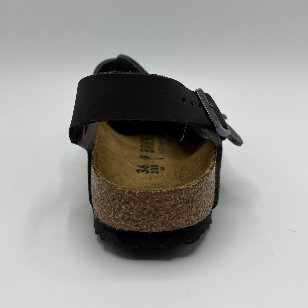 Back view of a charcoal slip on shoe with two adjustable buckle straps on a white background