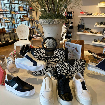 Black EOS Woven Sneaker along with other black and white sneakers on display in front of BOHO bags