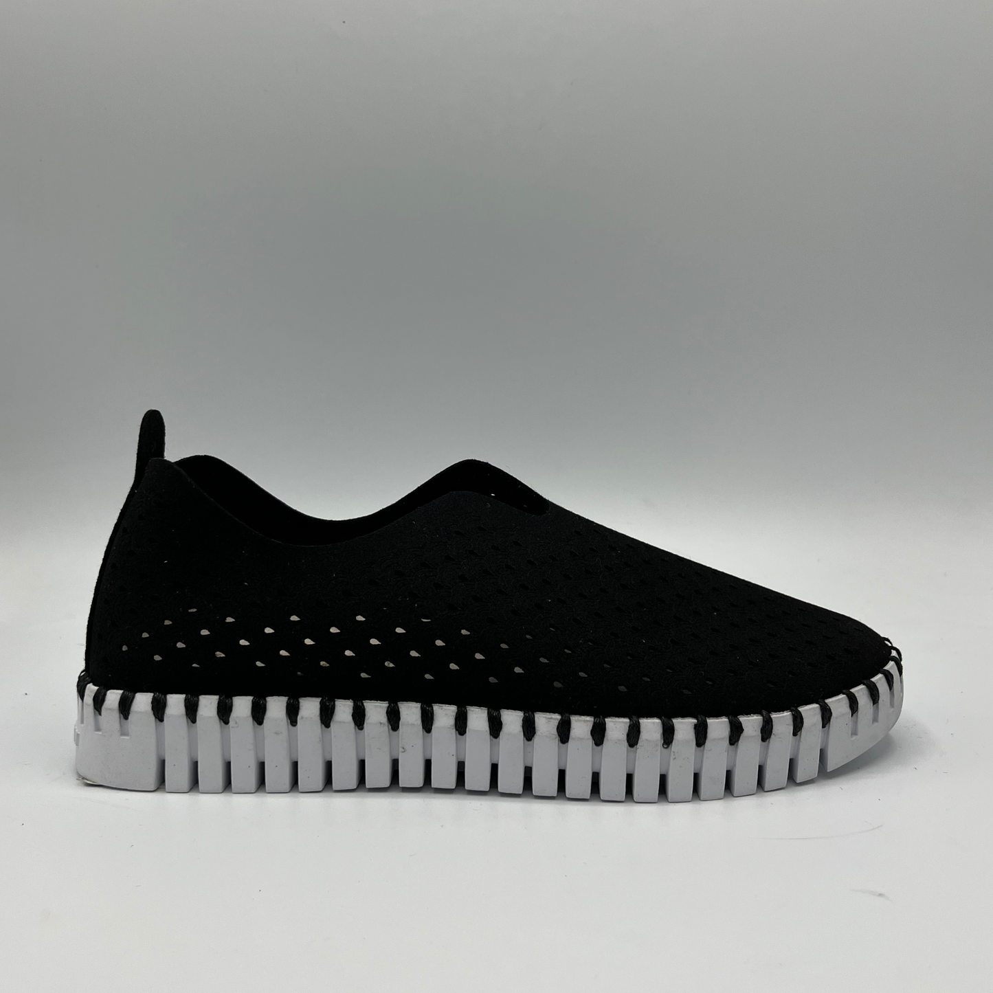 Right facing view of black slip on shoe with an intricate laser cut upper and white rubber outsole.