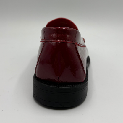 A glossy patent leather loafer shown from a rear three-quarter angle, featuring a deep burgundy red upper with matching red stitching and a chunky black sole, set against a plain light gray background.