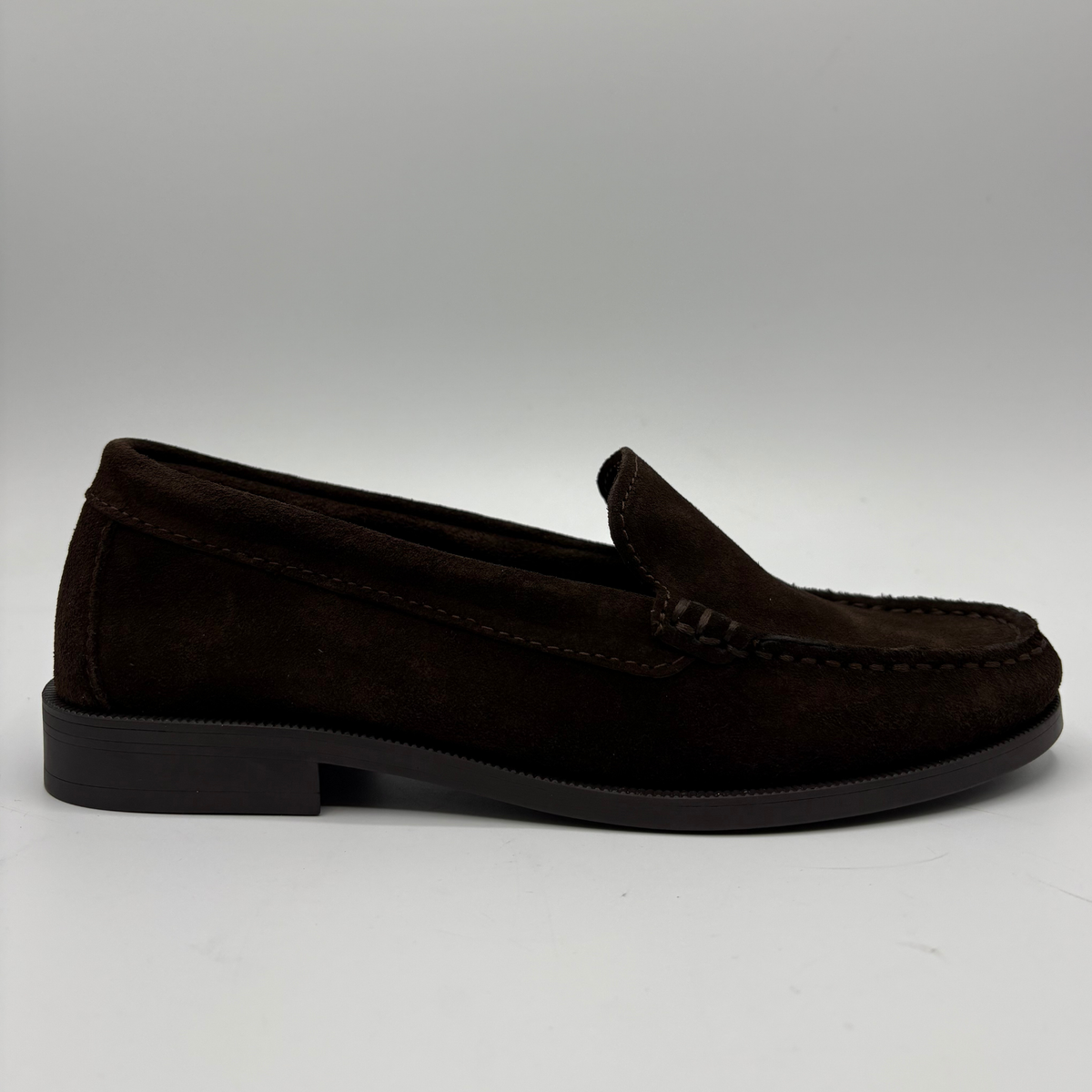 A dark brown suede moccasin loafer shown in a side profile view against a neutral gray background.