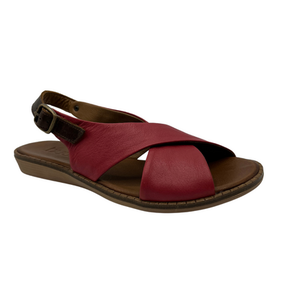 45 degree angled view of red leather sandal with cross strap design, slight wedge heel and brown slingback strap