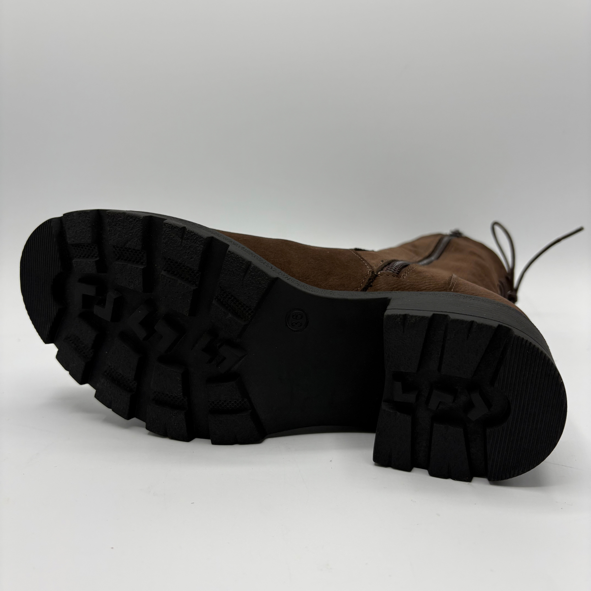 A brown suede lace-up boot shown from a low angle, displaying its black lug sole and tread pattern against a light gray studio background.