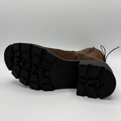 A brown suede lace-up boot shown from a low angle, displaying its black lug sole and tread pattern against a light gray studio background.