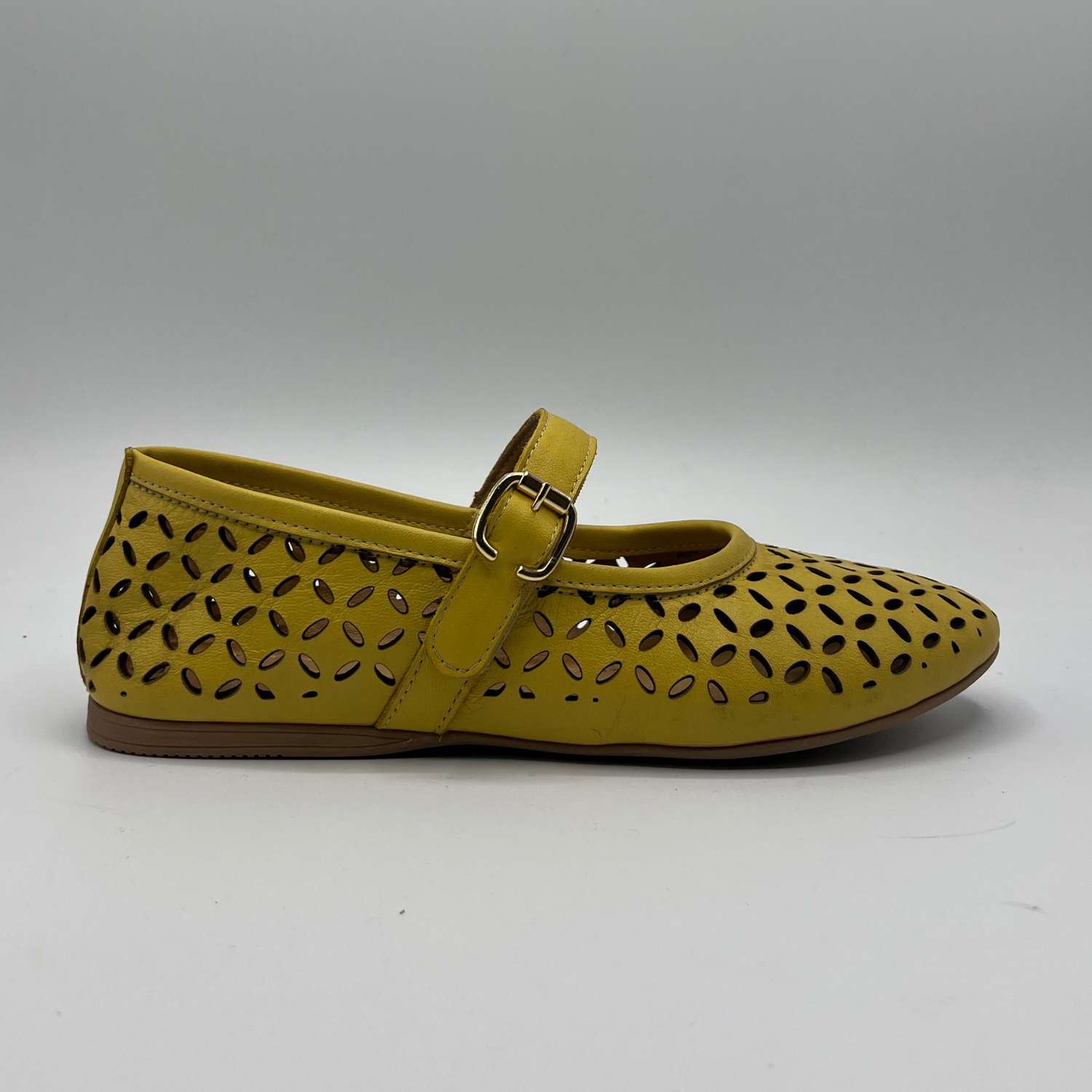 Right facing view of a yellow leather ballet flat with a laser cut design on the upper. Featuring an adjustable velcro strap with a decorative buckle.