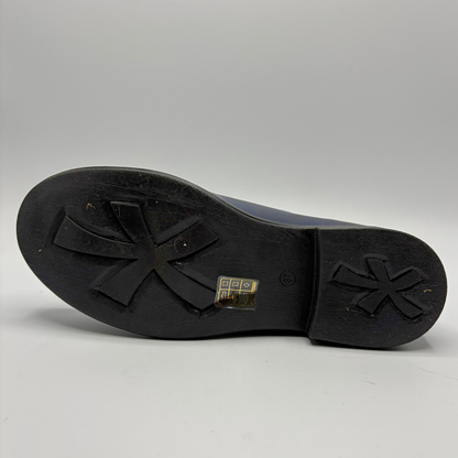 The black rubber outsole of a shoe, showing a distinctive four-pointed star-like tread pattern on the front and heel, with a small gold brand tag in the center.