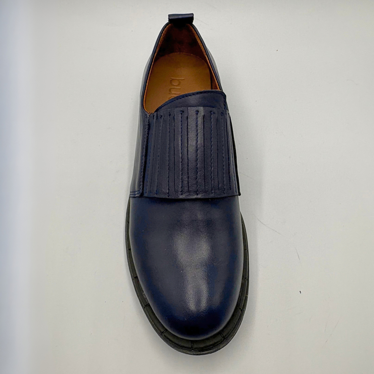 A single navy blue leather slip-on loafer with a vertical detail across the instep and a black sole, photographed from a top-down angle on a light gray background.