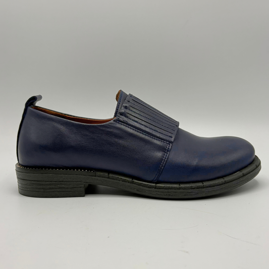 A single navy blue leather slip-on shoe with a decorative detail across the vamp and a low black sole, photographed against a neutral gray background.