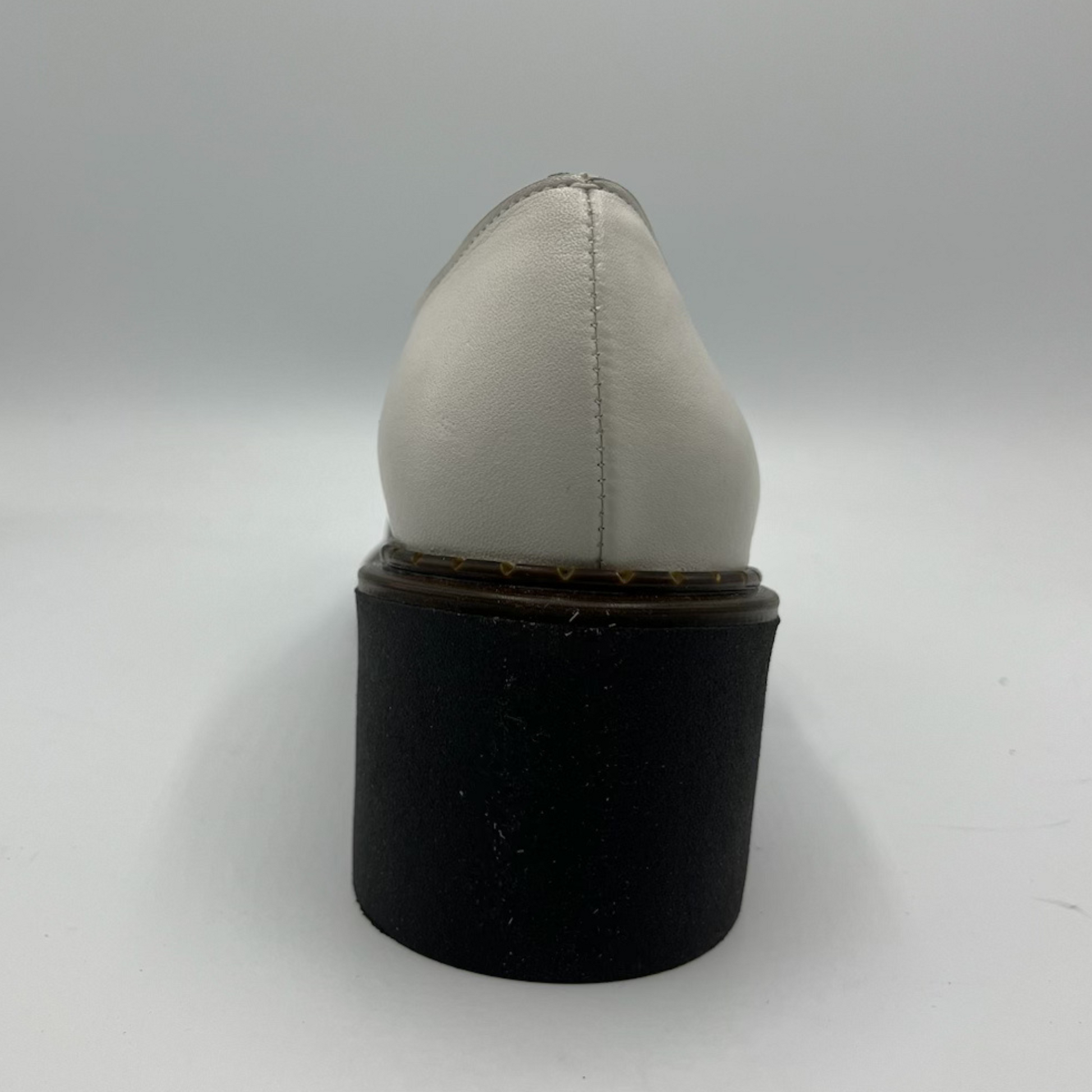 White shoe on a black cylindrical stand against a white background