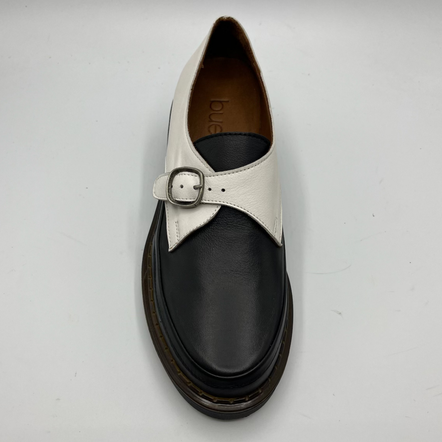 White and black shoe with a buckle on a light gray background