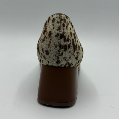 A single women's pump shoe shown from the back, featuring a brown and beige animal-print hair-on-hide upper and a solid dark brown block heel, set against a neutral gray studio background.