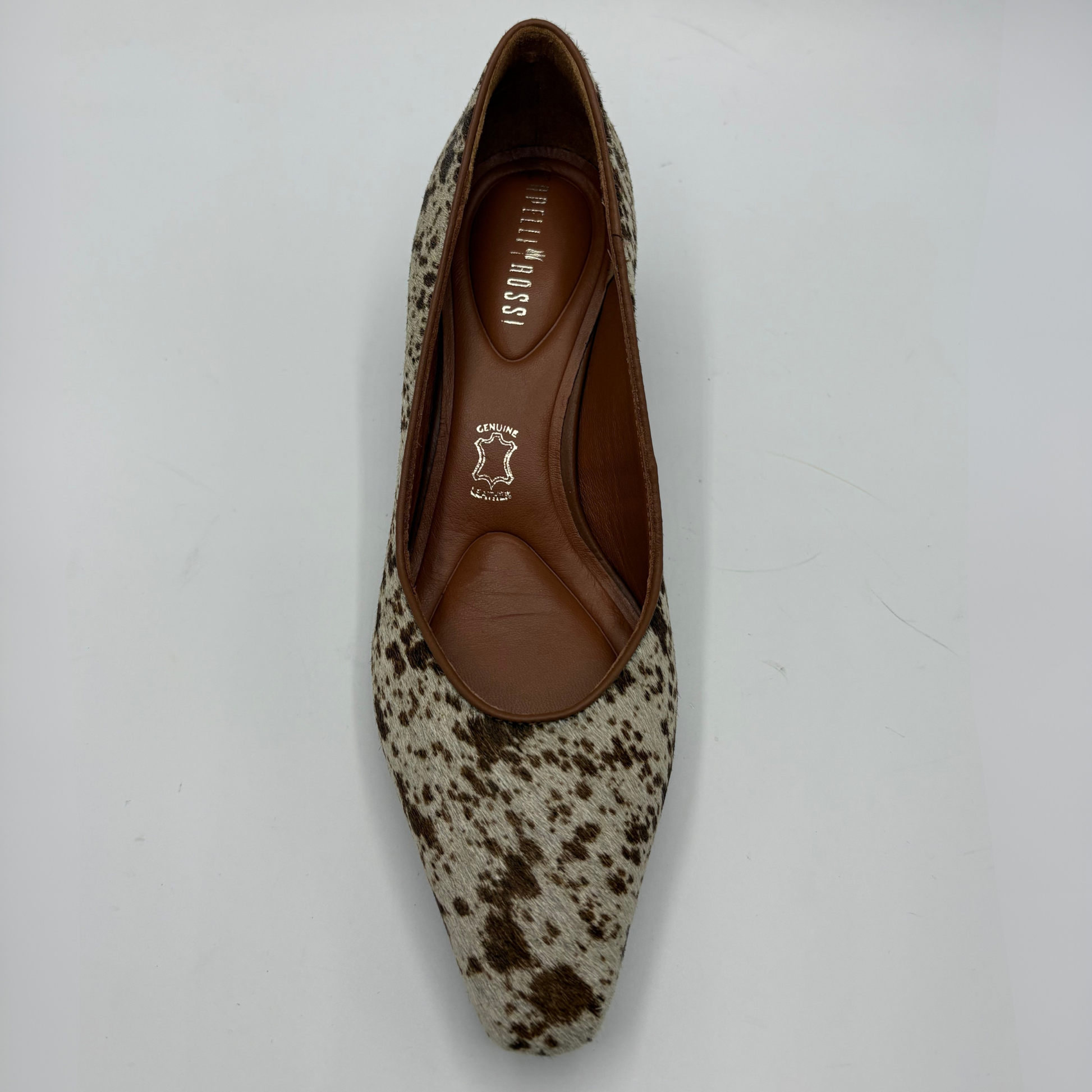 A single pointed-toe flat shoe with a brown and beige cowhide pattern, featuring a brown leather insole with the brand name printed on it, photographed from a top-down angle on a light gray background.